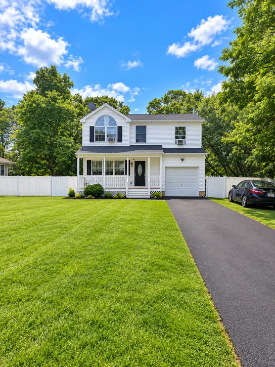 Mastic: A two-story New Roots home with a green lawn, a covered front porch, and a driveway.
