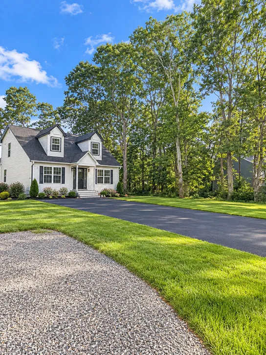 Shirley: The Shirley house with light siding, a dark front door, green lawn, driveway, and tall trees.